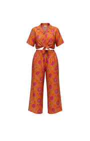 Ensemble Devï Studios SARL deux pièces en soie et viscose orange à imprimé floral rose et vert, chemise courte nouée et pantalon large.