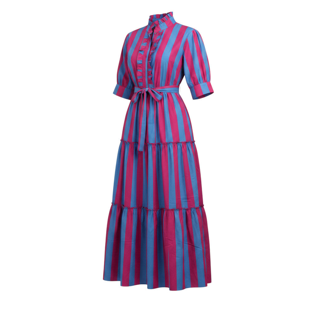 Robe longue Annick Devï Studios SARL en coton bleu et rose à rayures, col haut, manches courtes, ceinture à la taille, jupe à volants. Femme tenant un bébé.