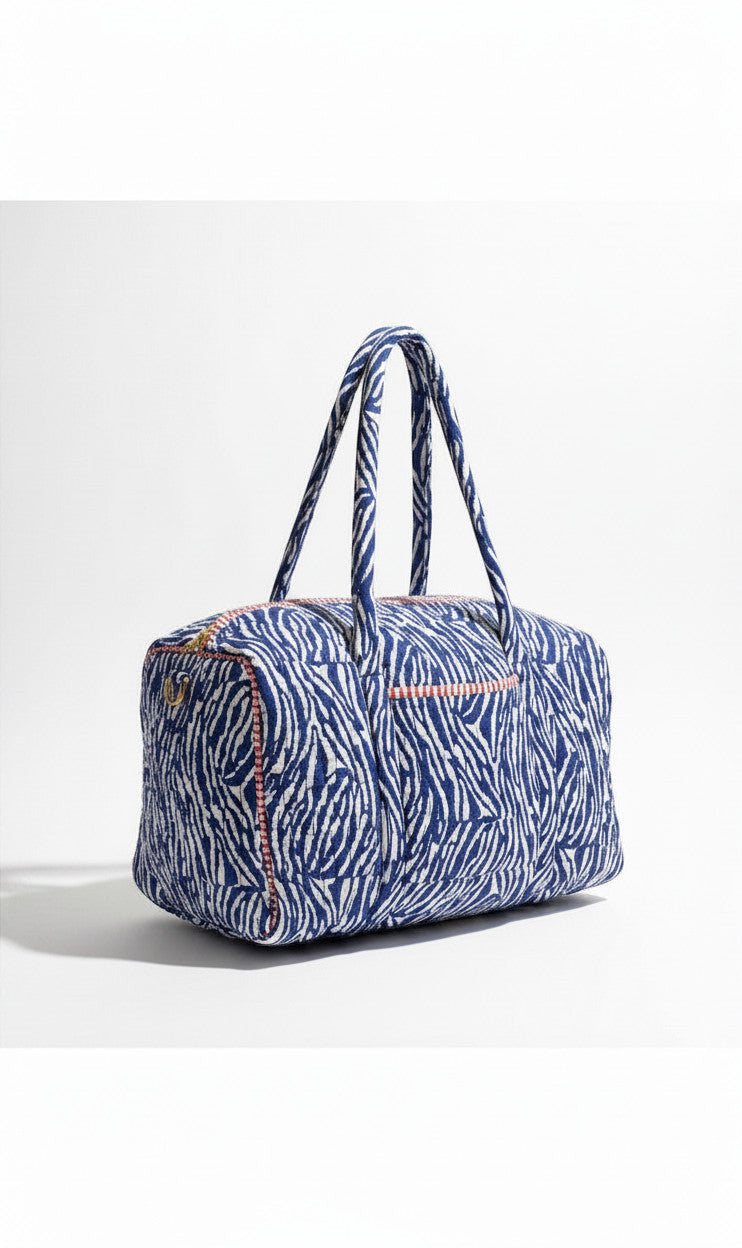 Sac de voyage Devï Studios SARL Isabella en coton bleu et blanc à motif zèbre, anses courtes et garniture rose.