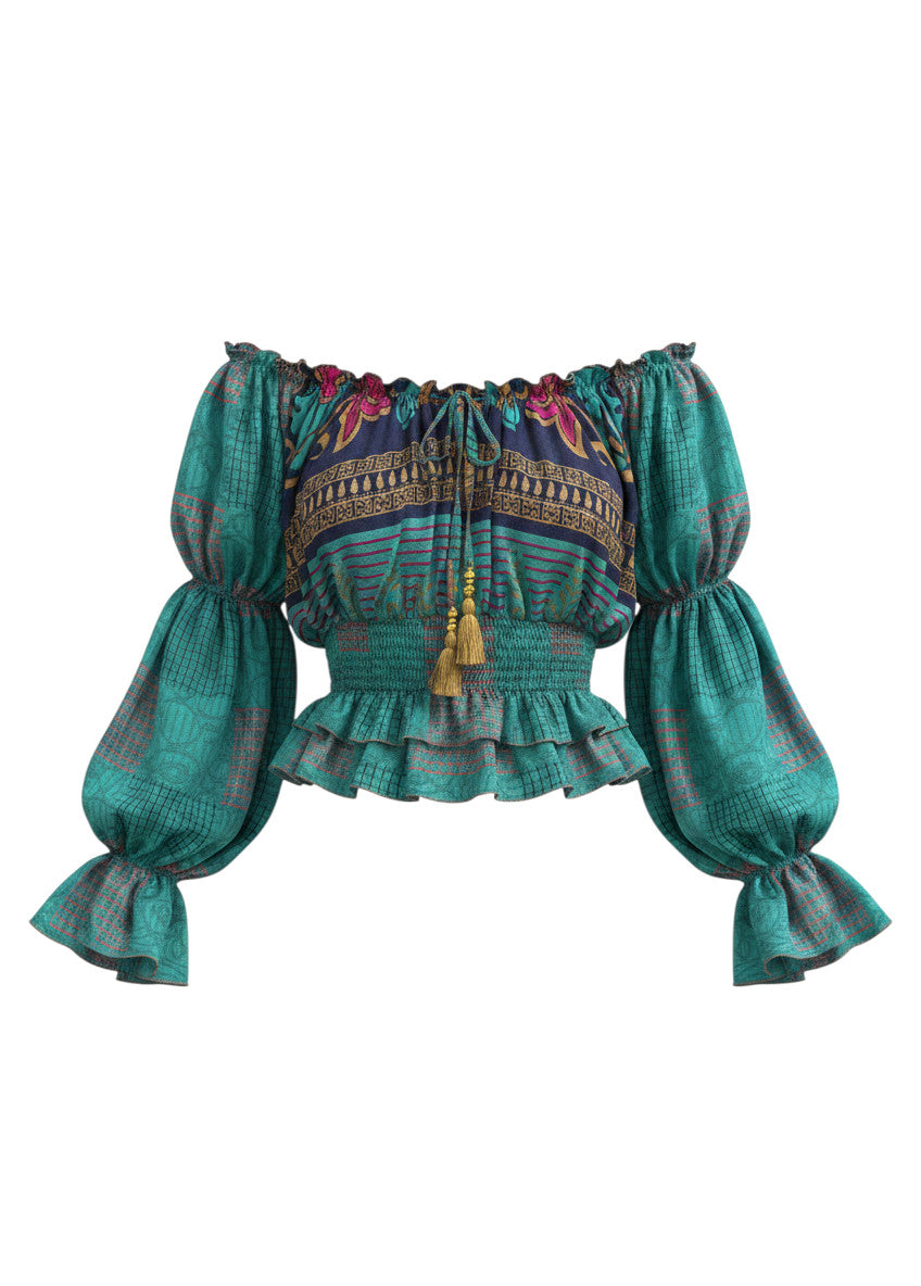Top Sari Nora Devï Studios SARL bleu turquoise à imprimés ethniques, manches longues bouffantes, col froncé avec liens et pompons, taille élastiquée, 70% soie, 30% viscose.